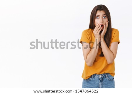 Scared, shocked timid insecure woman standing speechless, drop jaw, gasping stare camera frightened, hear stunning rumours, holding hands on mouth horrified, standing white background