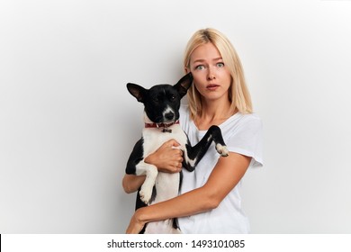 Scared Shocked Woman Carries Lovely Dog, Dressed In White Stylish T-shirt, Has Free Time, Isolated On White Studio Wall, Close Up Portrait, Facial Expression, Reaction