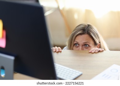 Scared and shocked woman in panic behind desk looking at computer screen. Getting bad news, watching scary movie and problem with computer concept.