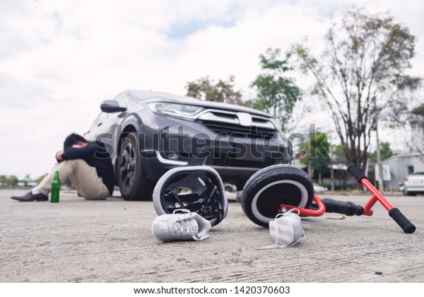 scared and stressed desperate drunken driver
and bottle of beer in front of automobile crash car with child bike
after traffic accident in city
road