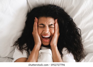 Scared Stressed Young African Girl Crying In Her White Bed. Top View Of Dark Skinned Woman Scared Of Nightmare, Lies In Bed With White Bedclothes, Afraids Of Staying Alone, Slept Bad At Night