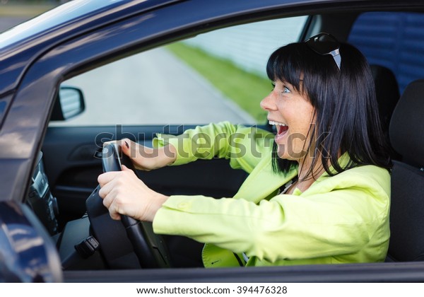 Scared and\
surprised woman with big eyes holds the steering wheel with both\
hands shouts driving the car -\
outdoors