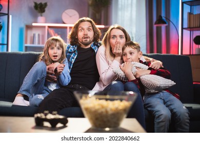 Scared or surprised young parents with little son and daughter watching horror breathtaking movie on TV during evening time at home. Real human emotions. Family leisure concept. - Powered by Shutterstock