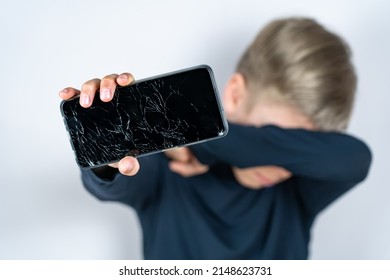 Scared Teen Boy With Emotional Expression Showing Broken Smartphone. Portrait Frustrated Kid With Broken Mobile Phone Screen, Shocked With Shame For Mistake, Expression Of Fear