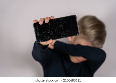 Scared Teen Boy With Emotional Expression Showing Broken Smartphone. Portrait Frustrated Kid With Broken Mobile Phone Screen, Shocked With Shame For Mistake, Expression Of Fear