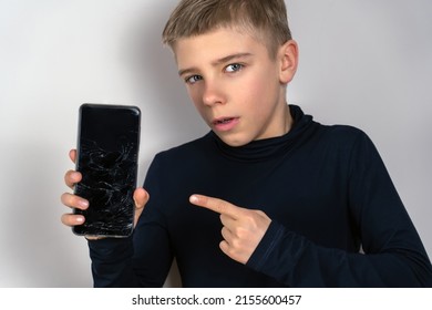 Scared Teen Boy With Emotional Expression Showing Broken Smartphone. Portrait Frustrated Kid With Broken Mobile Phone Screen, Shocked With Shame For Mistake, Expression Of Fear