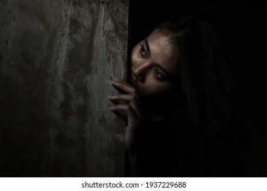 Scared woman hiding behind wall in dark room Young crazy scared and shocked asian woman escape murderer and get frightened Copy space Facial expression, human emotion and halloween concepts copy space