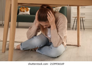 Scared Woman Hiding Under Table In Living Room During Earthquake