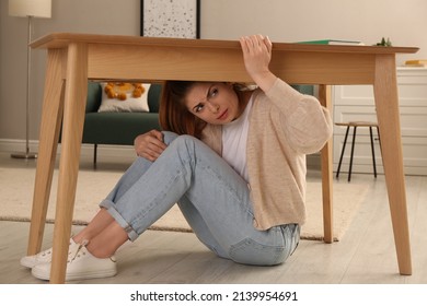 Scared Woman Hiding Under Table In Living Room During Earthquake