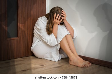 Scared woman with schizophrenia sitting in the corner at room with people shadows - hallucinations and schizophrenia disease concept