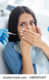 Scared Woman Sitting In Dental Chair Covering Mouth With Hands