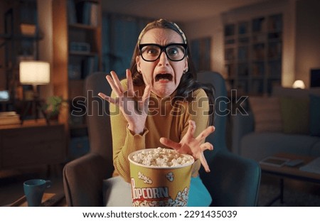 Scared woman watching a terrifying horror movie on TV and eating popcorn