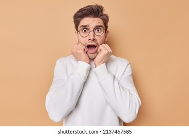 Scared Worried Man Stares Bugged Eyes Keeps Mouth Opened Afraids Of Something Terrifying Canot Believe In Horrible News Wears Casual White Jumper Isolated Over Beige Background. Human Reactions