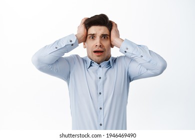 Scared and worried office manager, man in shirt panicking, holding hands on head and look nervous, standing over white background