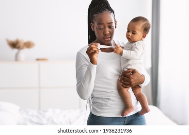 Scared young African American mother looking at thermometer - Powered by Shutterstock