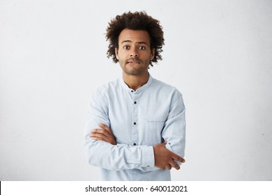 Scared young Afro American man in casual shirt keeping arms folded, biting lips, feeling nervous and impatient while waiting for his wife giving life for their first child. Human emotions and feelings