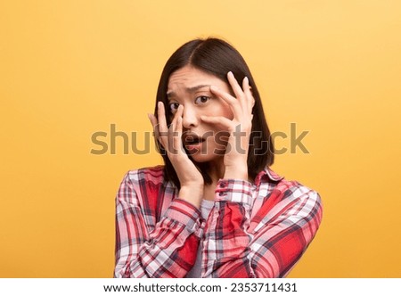 Scared young chinese lady student in casual outfit covering her face with hands and afraid, standing isolated on yellow background. Human emotions, facial expression and bad news