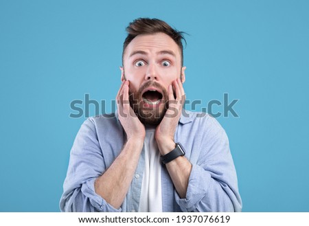 Scared young guy screaming in panic over blue studio background
