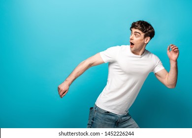 Scared Young Man Running Away And Looking Back On Blue Background