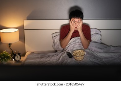 Scared Young Man Is Watching Horror Movie TV On A Bed At Night