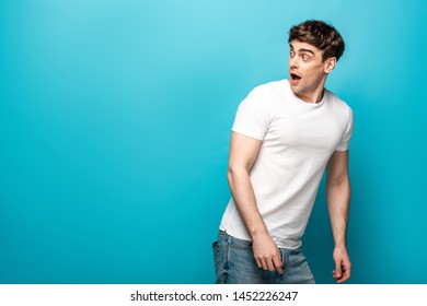 Scared Young Man In White T-shirt Looking Back On Blue Background