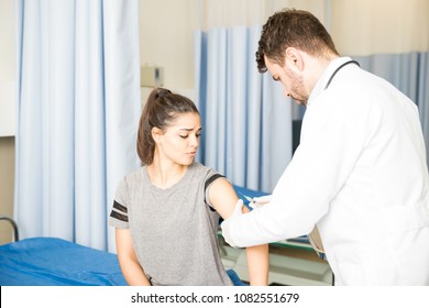 Scared Young Woman Getting A Vaccine Shot On Her Arm By Male Doctor At Clinic