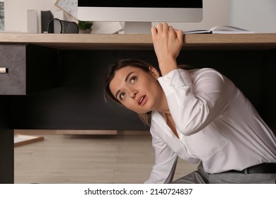 Scared Young Woman Hiding Under Office Desk During Earthquake