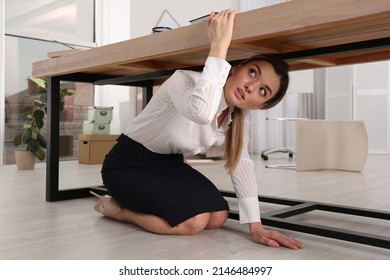 Scared Young Woman Hiding Under Office Desk During Earthquake