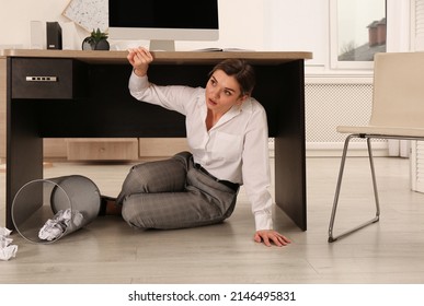 Scared Young Woman Hiding Under Office Desk During Earthquake