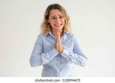 Scared young woman holding hands together and begging. Upset curly-haired female employee praying and asking about forgiveness. Despair concept