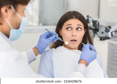 Scared Young Woman Looking At Dentist With Eyes Wide Open, Doctor Holding Tools, Fear Of Dentistry Concept