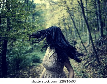 Scared young woman running through a forest at night, looking back