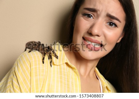 Scared young woman with tarantula on beige background. Arachnophobia (fear of spiders)
