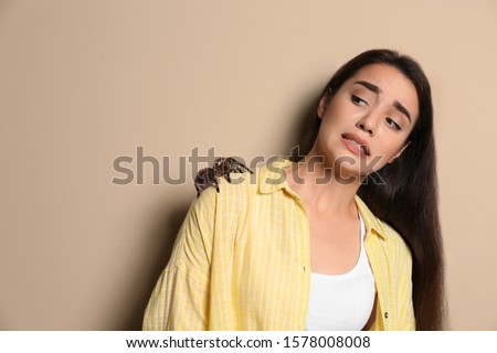 Scared young woman with tarantula on beige background. Arachnophobia (fear of spiders)