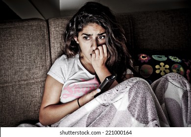 Scared Young Woman Watching Tv. Brunette Girl Sitting On Couch With Remote Control