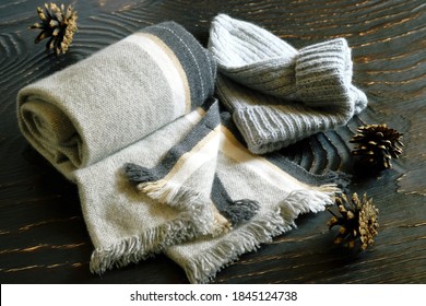 Scarf and knitted hat in gray, pine cones close-up on a dark wooden surface.