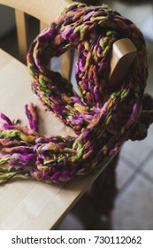 A scarf made of brown, pink, yellow, orange and green thread.