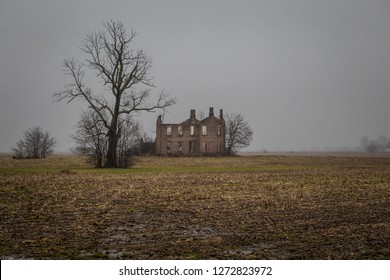 Scary Abandoned Mansion Next To Barren Tree In Field On Overcast And Foggy Day