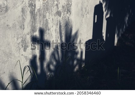 Scary abstract blurred moonlight shadows of grave cross and tombstones on abandoned wall on a cementery as concept background for Halloween