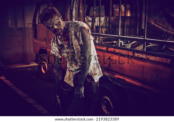 A scary bloody zombie stands by a broken\
car in a deserted city illuminated by a red bloody sunset. Zombie\
apocalypse. Halloween. Horror movie.\
