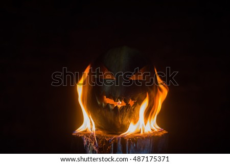 Scary carved halloween pumpkin in hot burning hell fire flames. The big helloween pumpkin has a mad face with glowing eyes and also a glow in its mouth and teeth. 