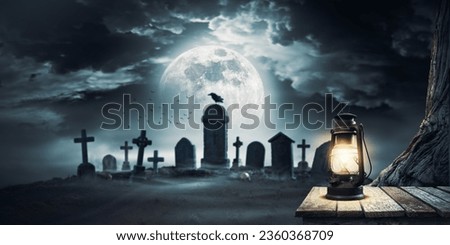Scary cemetery with ancient graves and old lit lantern in the foreground