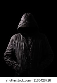 Scary And Creepy Man Hiding In The Shadows, With The Face And Identity Hidden With The Hood, And Standing In The Darkness. Low Key, Black Background. Concept For Fear, Mystery, Danger, Crime, Stalker