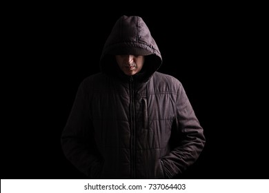 Scary and creepy man hiding in the shadows, with the face and identity hidden with the hood, and standing in the darkness. Low key, black background. Concept for fear, mystery, danger, crime, stalker
