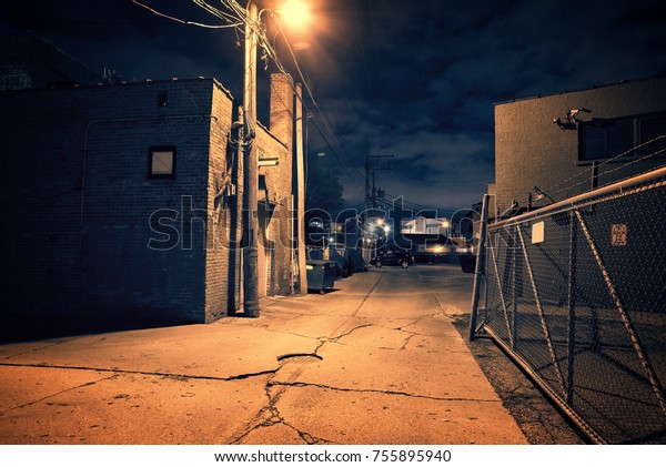 Scary dark city Chicago alley next to an urban\
warehouse and parking\
lot.