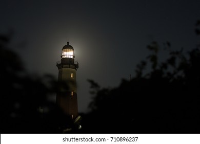 Scary dark ominous lighthouse illuminated by a brightly moon shine, starry night sky behind a blurred black bush.