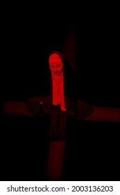 Scary devilish possessed nun with a cross in her hands kneels and prays standing in a dark room. Horrors and Halloween.