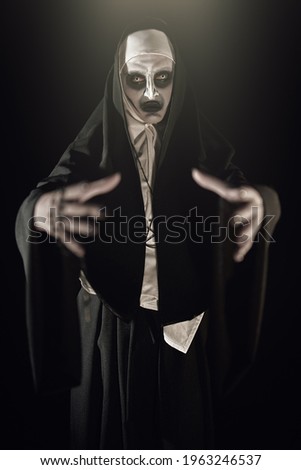 Scary devilish possessed nun holds out her hands in a dark room. Horrors and Halloween.