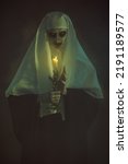 Scary devilish possessed nun standing with a candle in a dark room. Horrors and Halloween.