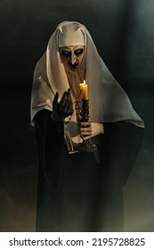 Scary devilish possessed nun standing with a candle in a dark room. Horrors and Halloween.